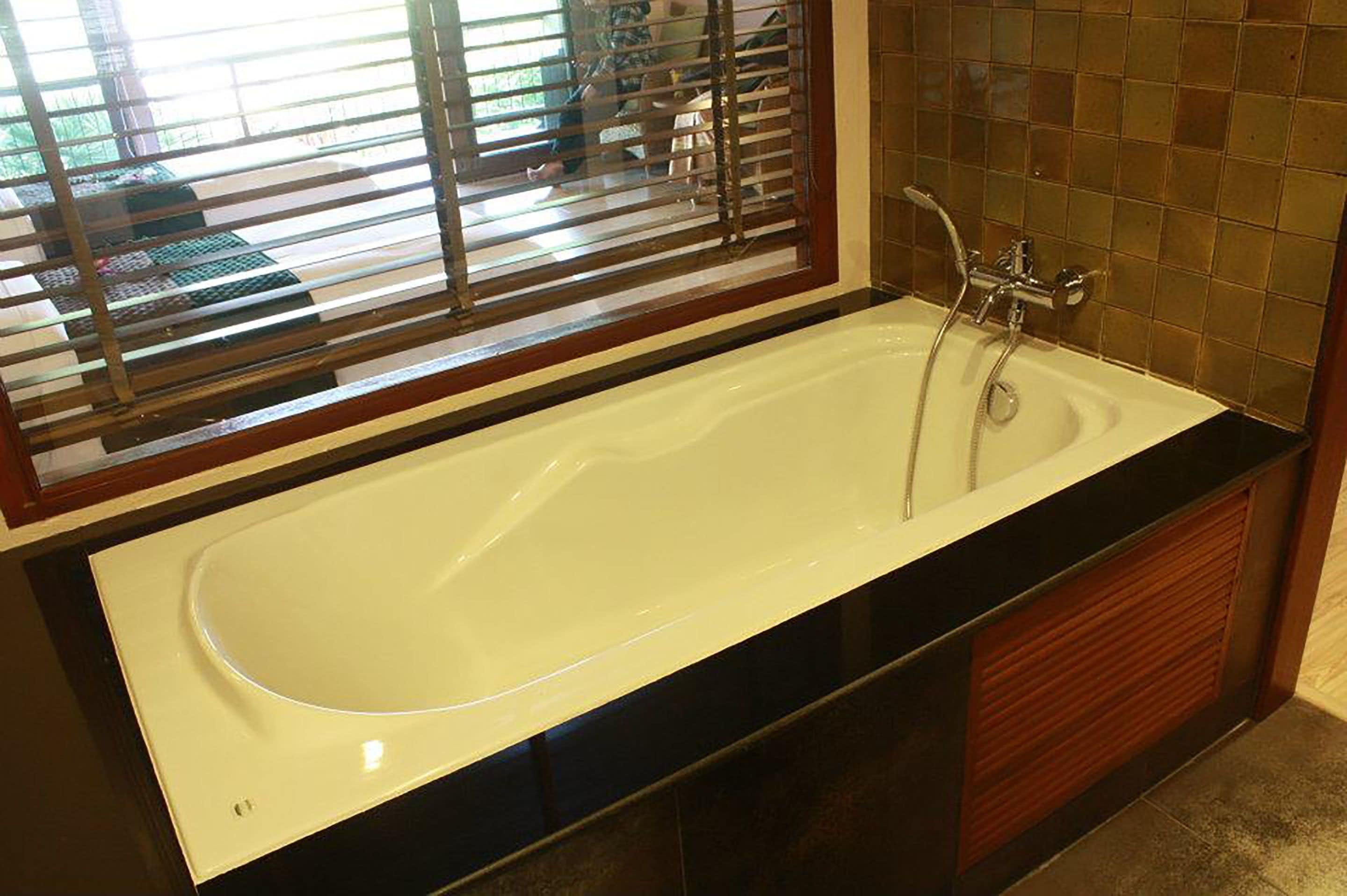 A large, white bathtub with a black countertop, a showerhead, and a window with blinds.
