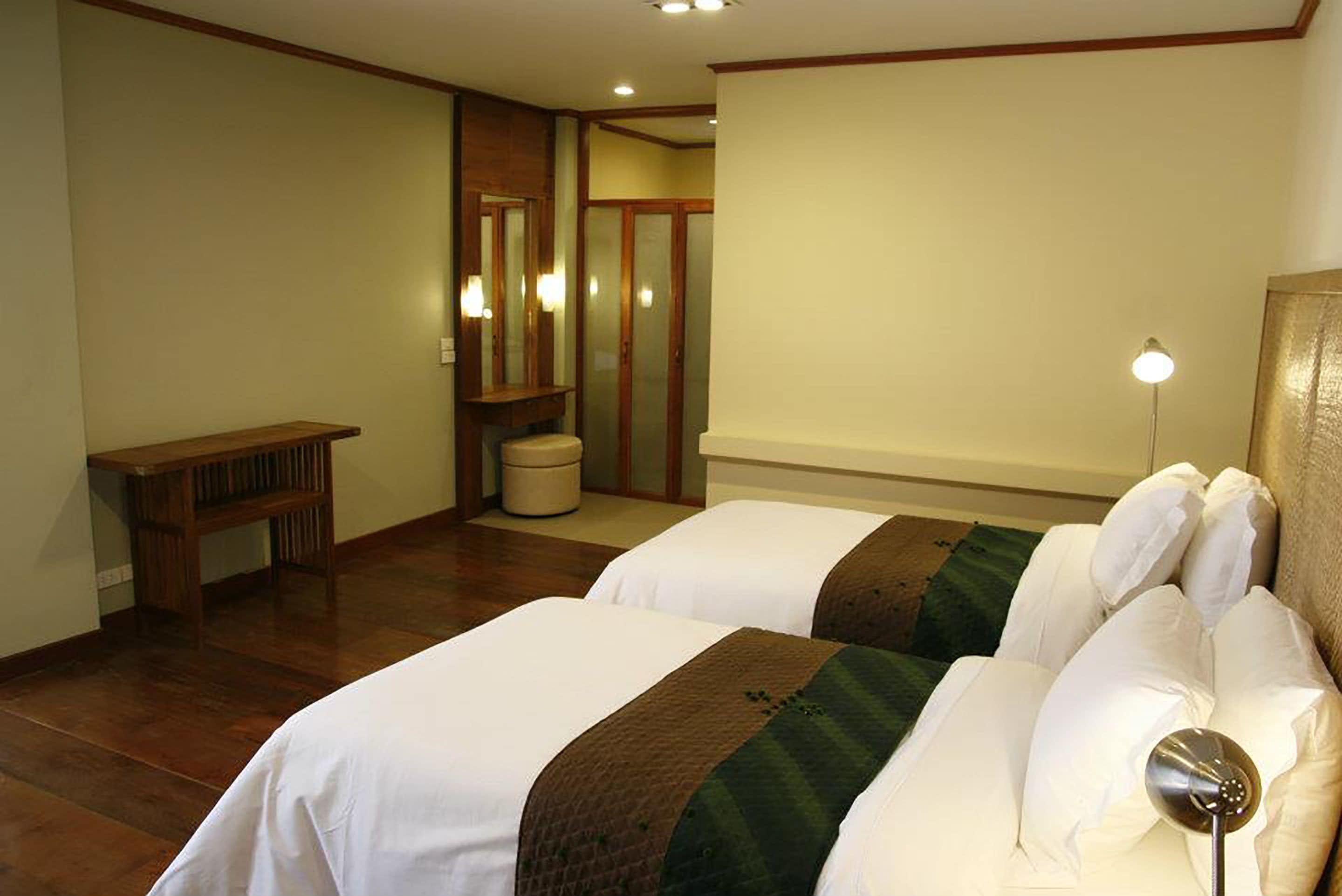 A hotel room with two beds, a bench, a mirror, and a trash bin.