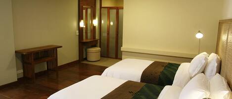 A hotel room with two beds, a bench, a mirror, and a trash bin.