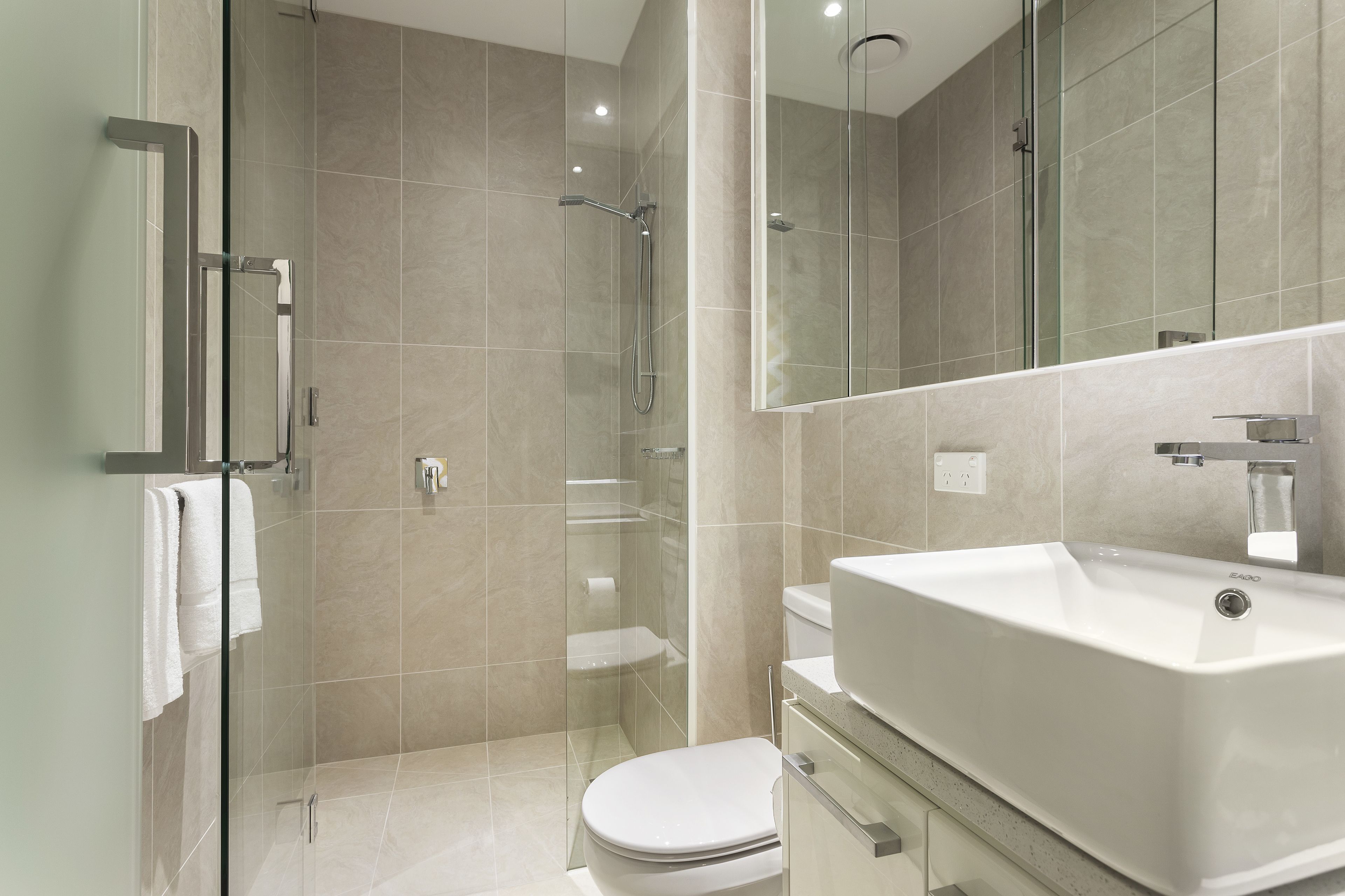 Un baño moderno con ducha envuelta en vidrio, inodoro blanco y un lavamanos grande.