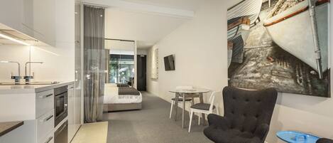 Una habitación de hotel moderna con kitchenette, una cama, un comedor y una obra de arte grande en la pared.