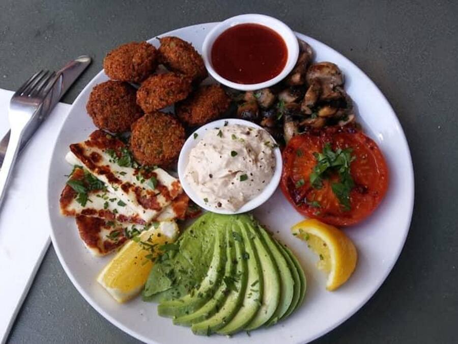 Un plato con falafel, hummus, tomates a la parrilla, rebanadas de aguacate y cuartos de limón.