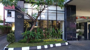 A modern building with a large glass window, a black and white curb, and a tree in the foreground. - Travello Manado (Manado)