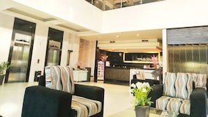A modern hotel lobby with a reception desk, two sofas with striped cushions, a glass coffee table, and a decorative plant. - Travello Manado (Manado)