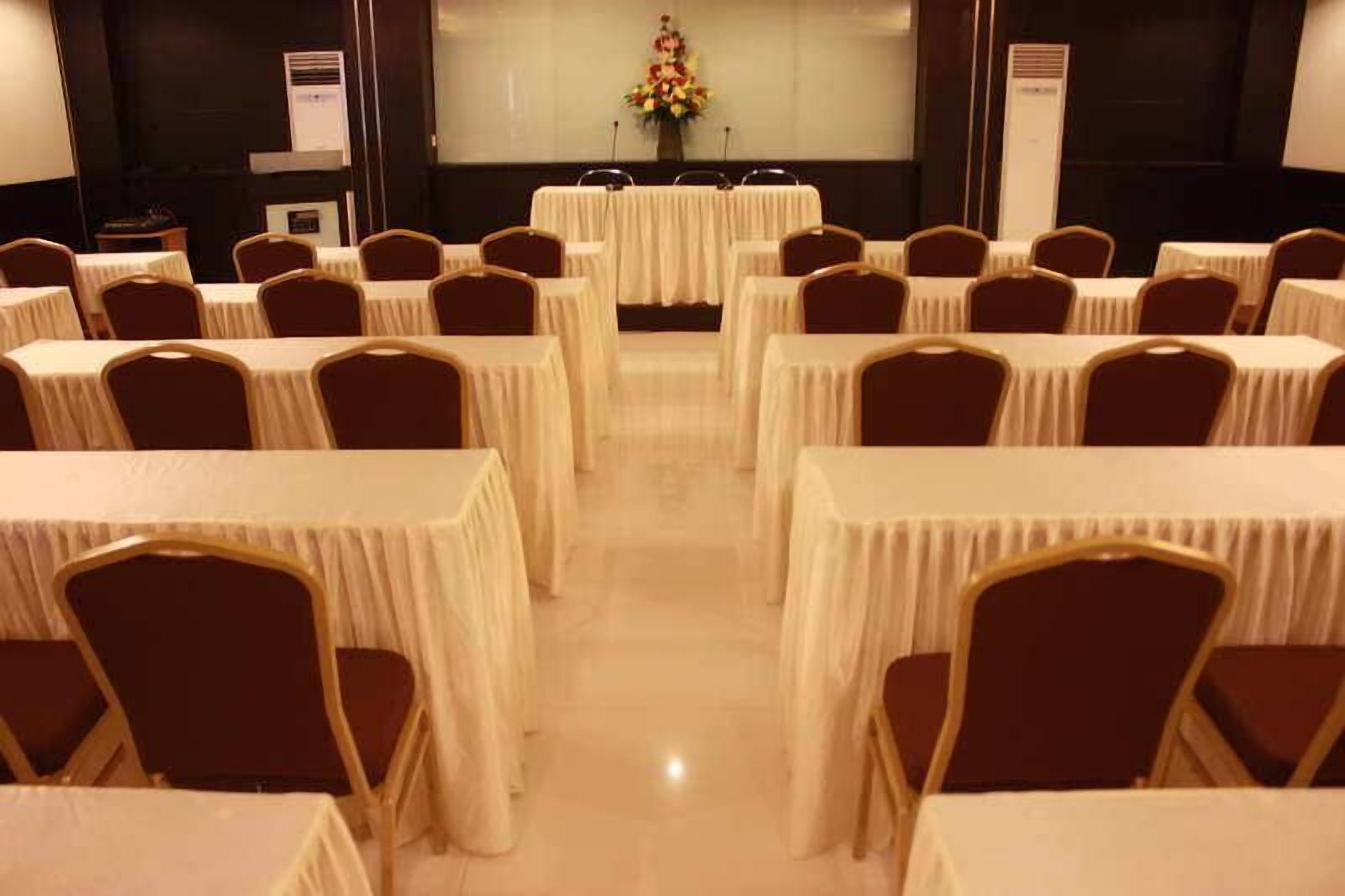 A conference room with rows of tables and chairs, a podium, and a floral arrangement.