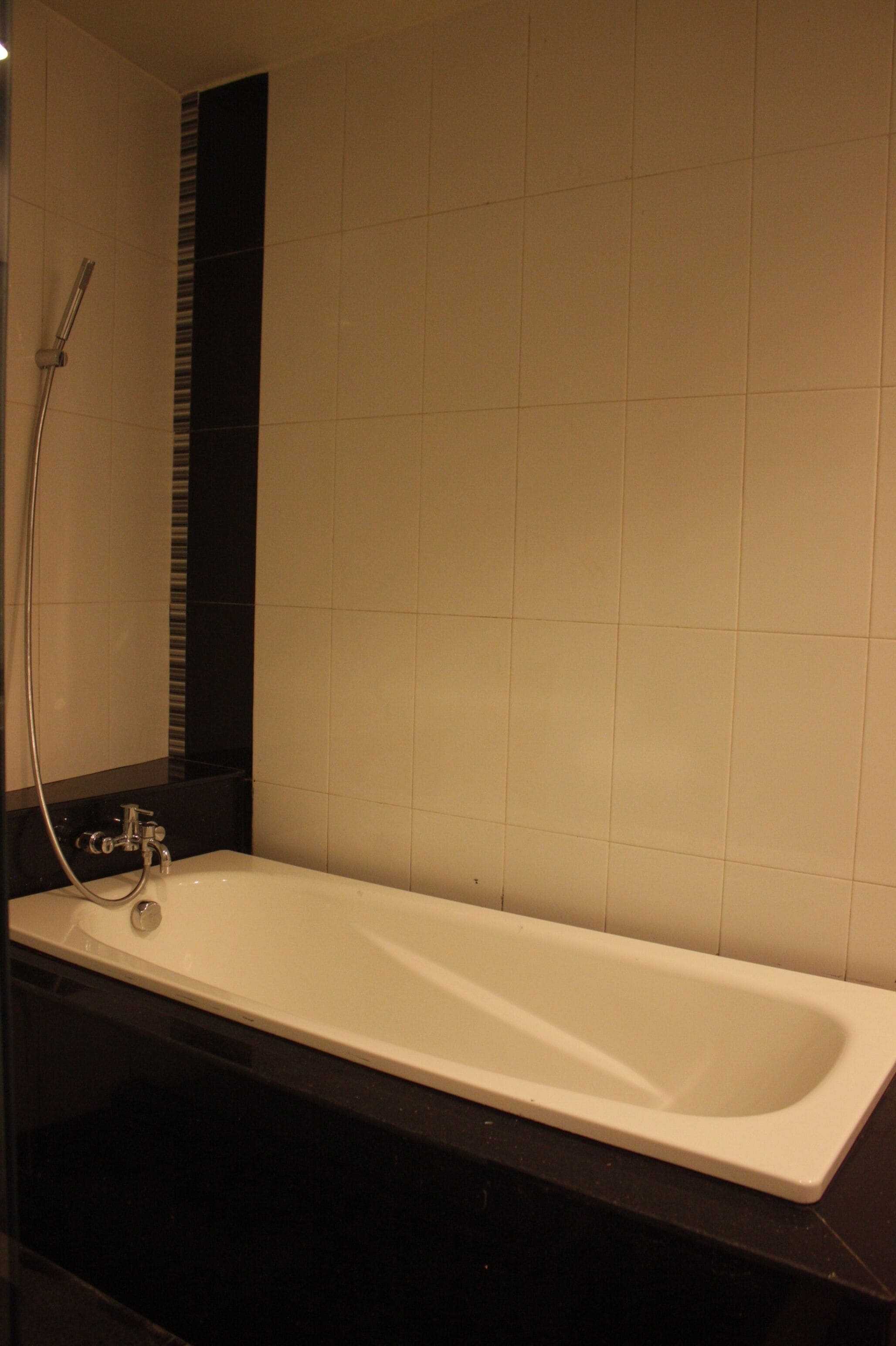 A modern bathroom with a white bathtub, a black countertop, and a tiled wall.