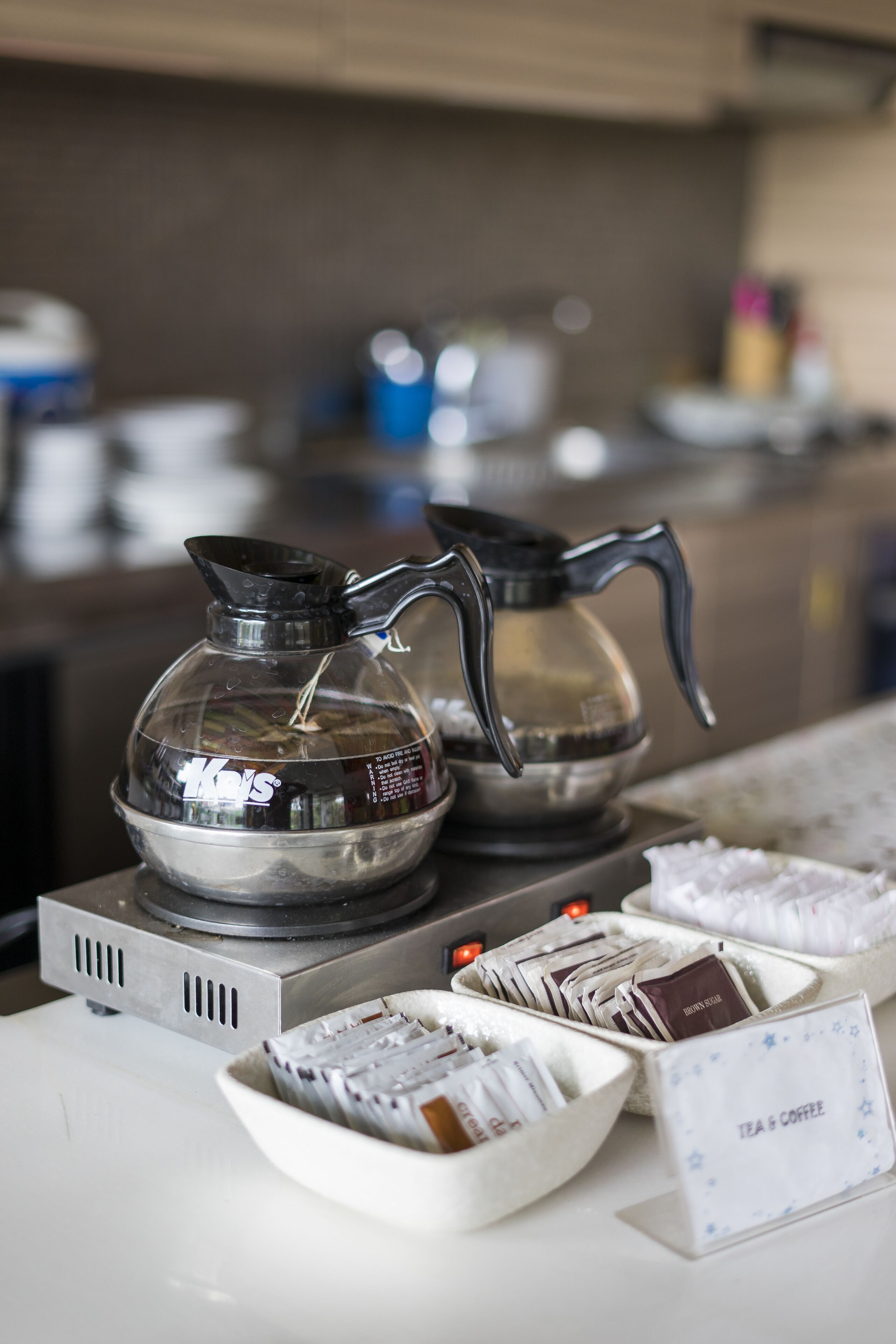 Un coin café comprenant une cafetière en verre, une bouilloire et un bol rempli de sachets de café.