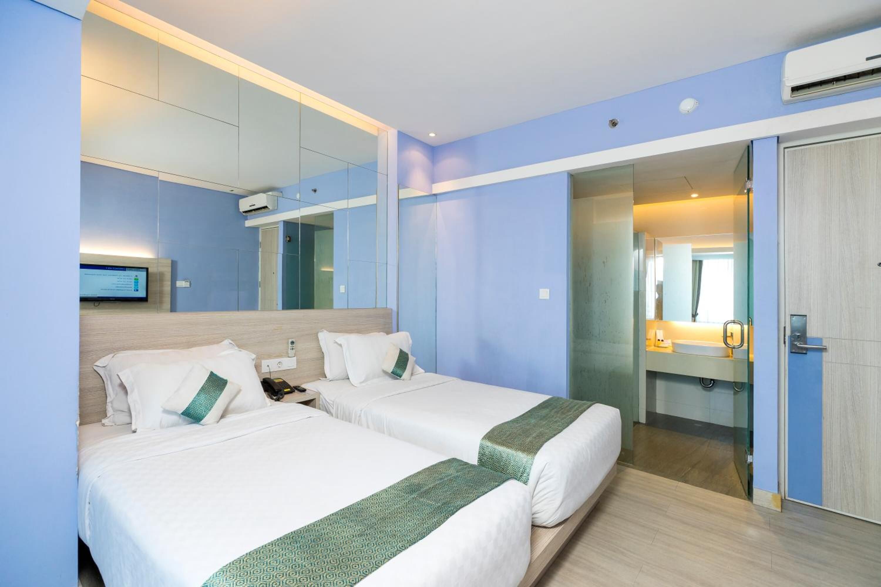 Une chambre d’hôtel avec deux lits, une télévision et une salle de bain avec un miroir, ainsi qu’une porte donnant sur une autre chambre.