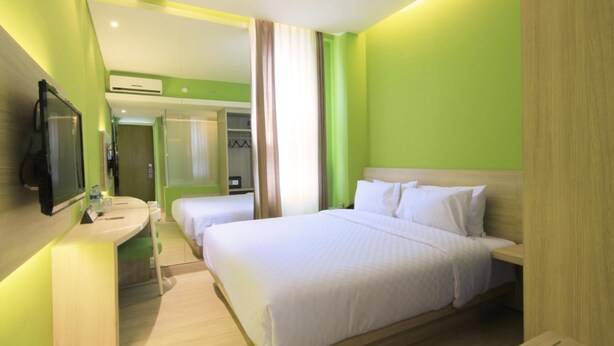 A hotel room with a bed, a bedside table, a mirror, and a bathroom with a sink and shower. - Royal City Hotel (Jakarta)