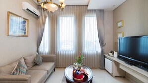 Un salon moderne comprenant un canapé, une table basse agrémentée d’objets décoratifs, un téléviseur à écran plat et une grande fenêtre avec des rideaux.