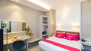 A hotel room with a bed, bedside lamps, a desk with a chair, a mirror, a shelf with toiletries, and a vase with flowers.