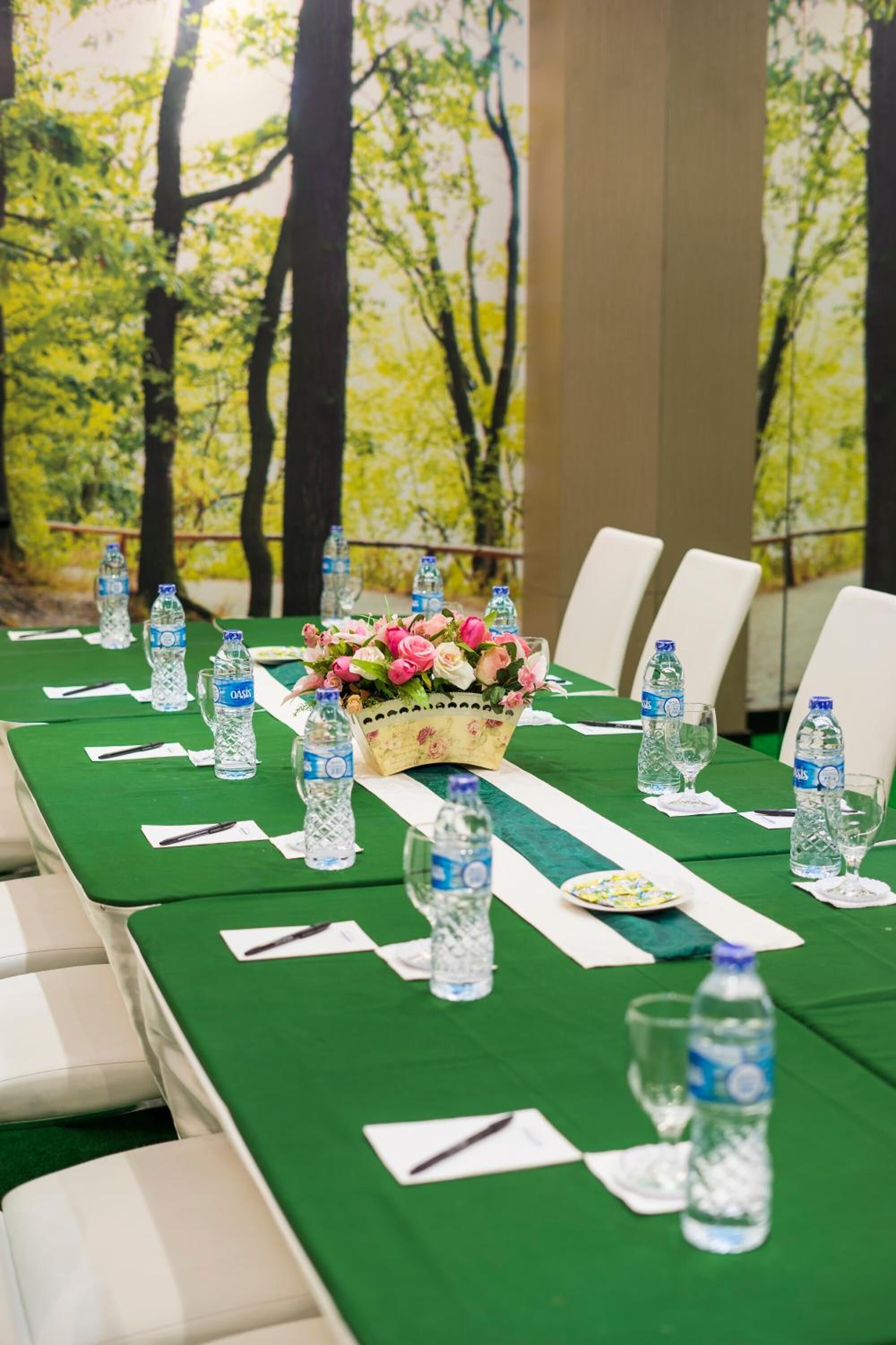 A conference table set with water bottles, a floral centerpiece, and white chairs.