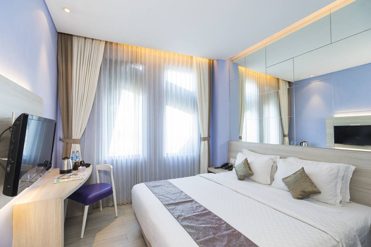 Een hotelkamer met een bed, een bureau met stoel, een televisie en een groot raam met gordijnen.