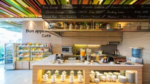 A café with a wooden counter, a menu board above it, and various food items displayed on shelves. - Royal City Hotel (Jakarta)
