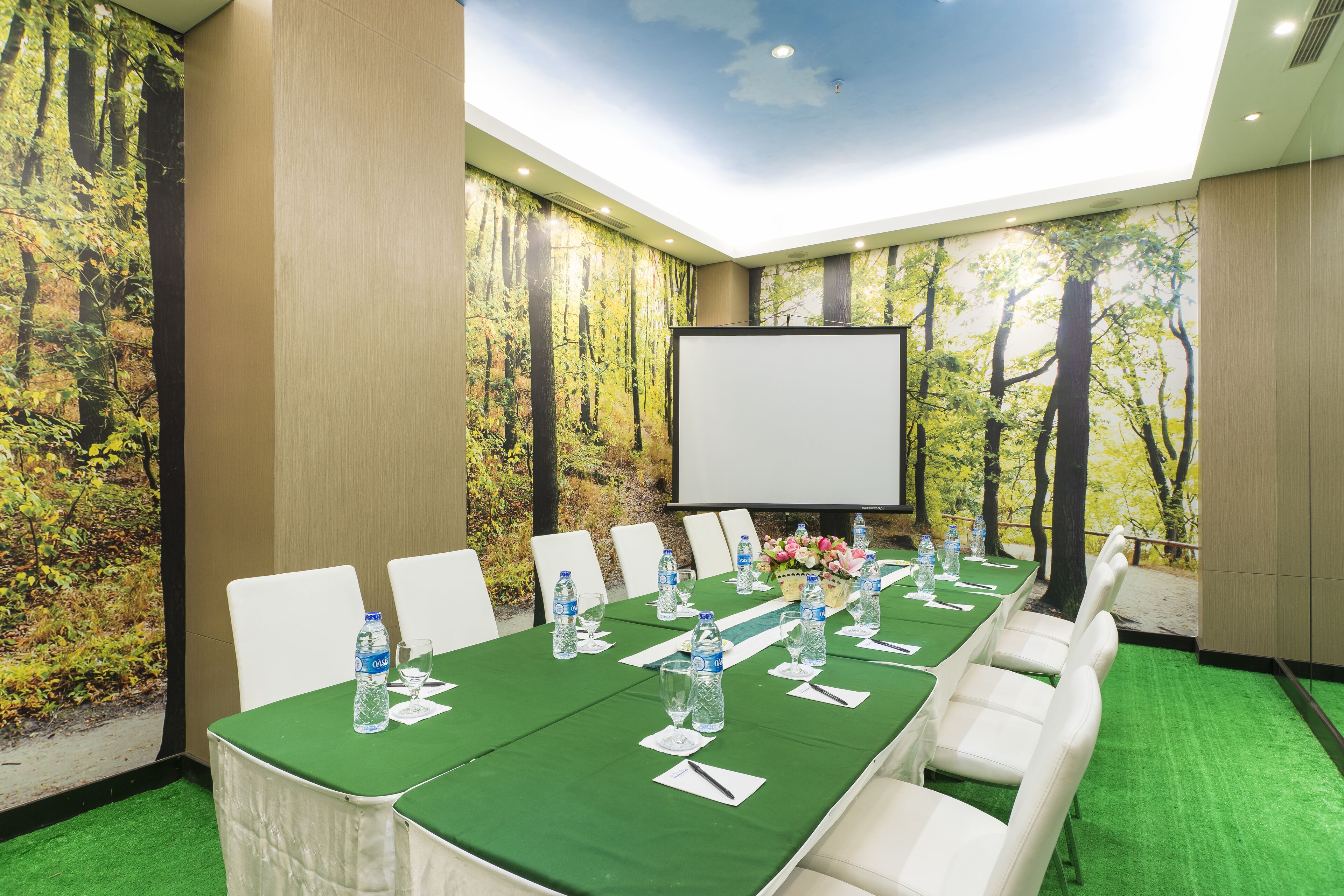 A conference room with a long table, white chairs, water bottles, and a projector screen.