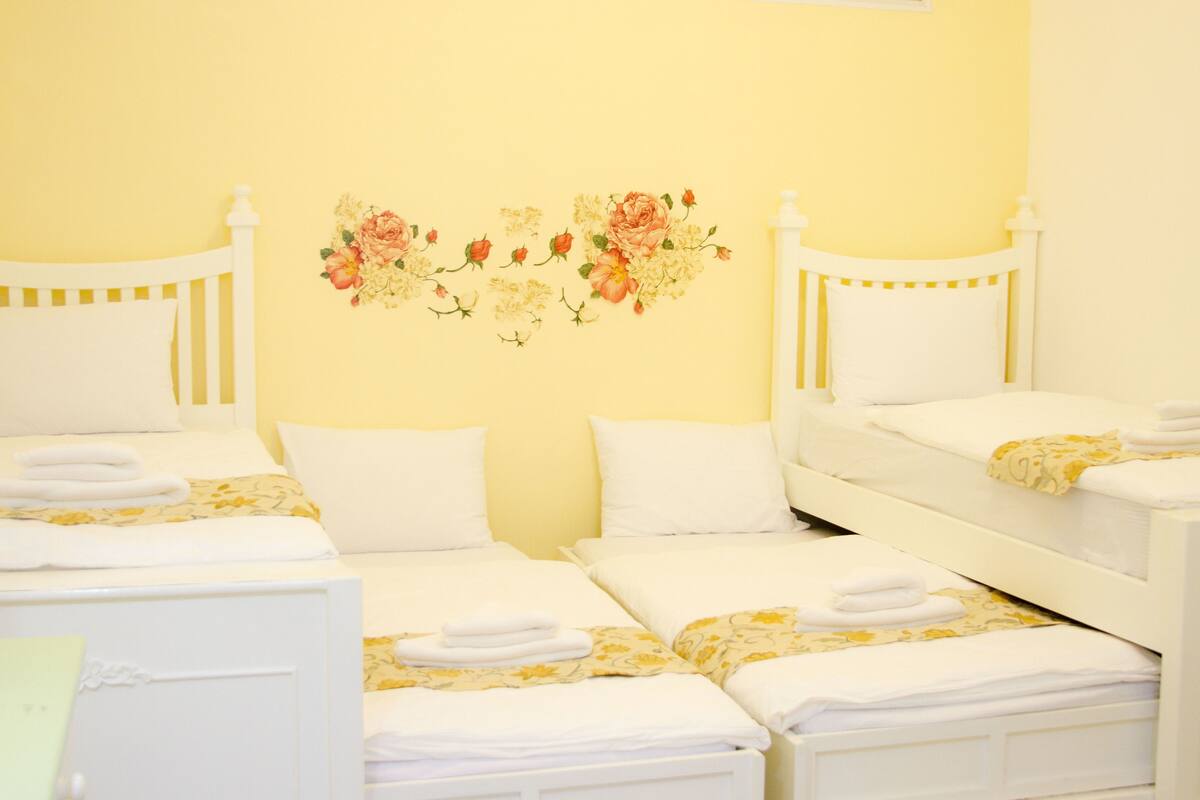 A hotel room with four single beds, each with white bedding and towels.