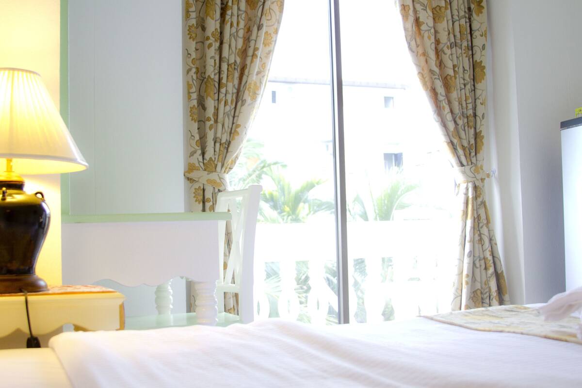 A hotel room with a bed, a lamp, a chair, and a window with curtains.