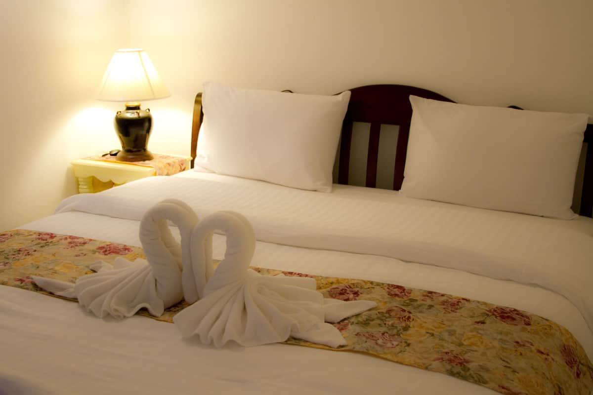 A neatly made bed with white linens and a floral bedspread. There is a lamp on a bedside table to the left.