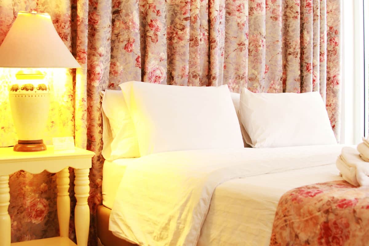 A hotel room with a bed, a nightstand with a lamp, and floral curtains.