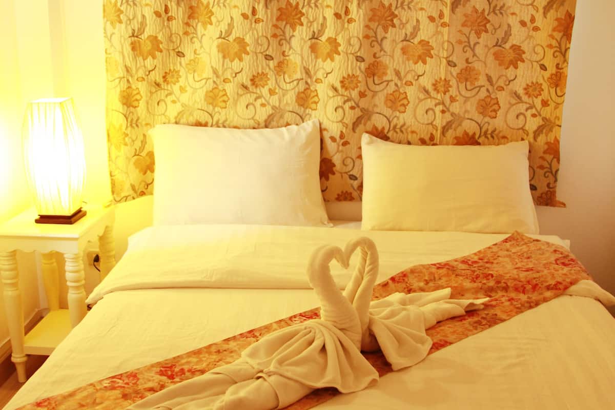 A hotel room with a bed, floral curtains, and a nightstand with a lamp.