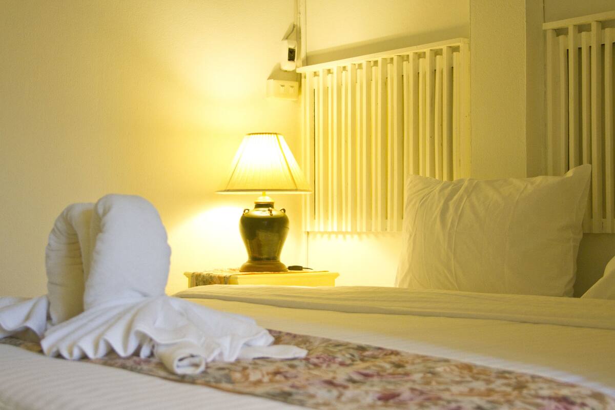 A neatly made bed with a floral bedspread, a bedside lamp, and white bedding.