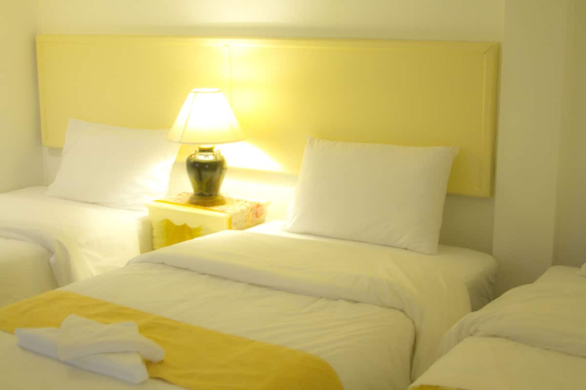A hotel room with two beds, a nightstand with a lamp, and a yellow towel on one bed.