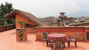 A terrace with a table and chairs, a potted plant, and a view of a town with buildings and mountains in the background. - World Heritage Hotel & Aparments (Kathmandu)