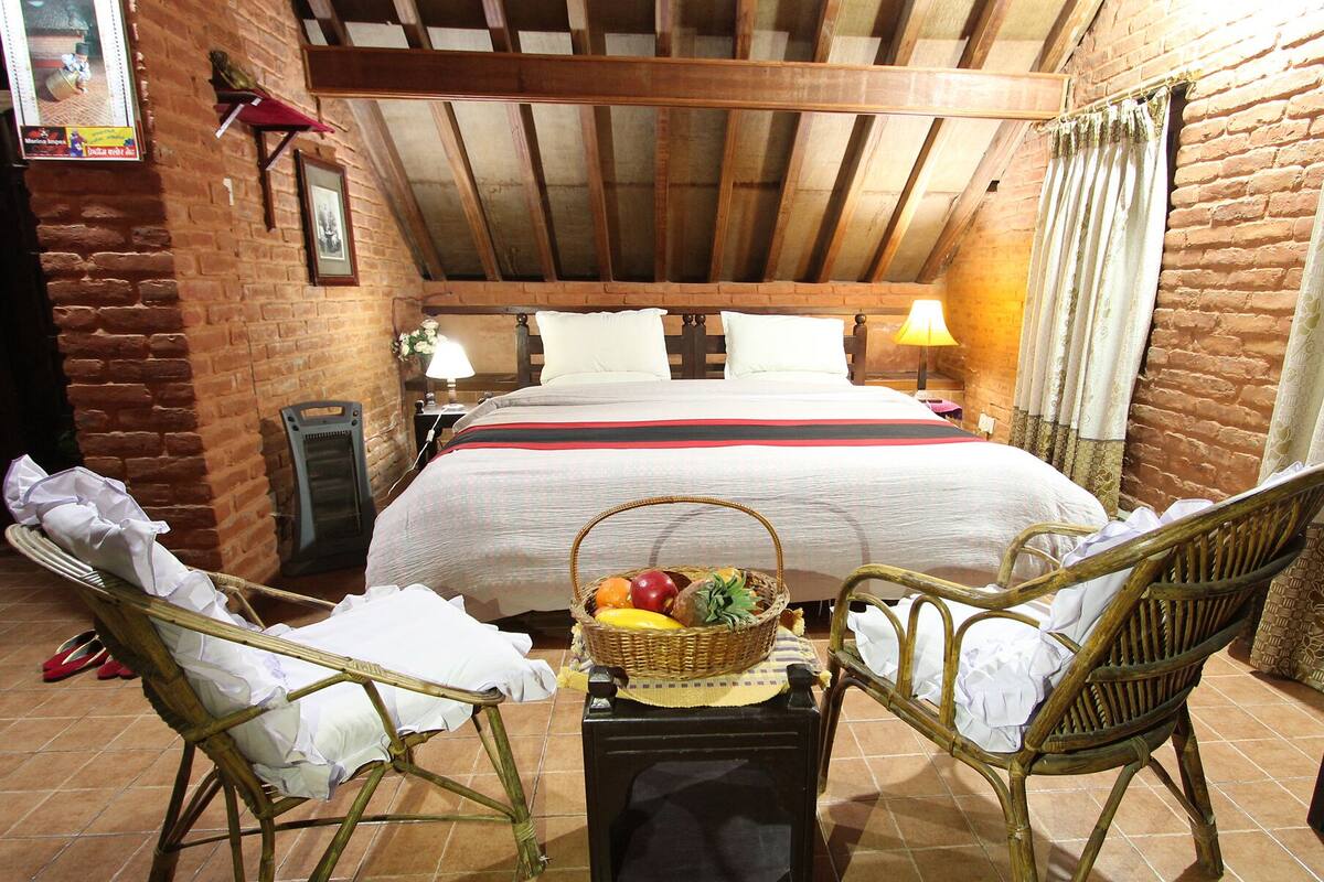 Een gezellige kamer met een bed, twee rieten stoelen, een kleine tafel met een fruitmand en een lamp.