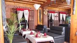 A cozy restaurant with wooden walls, red and white curtains, and black leather seating. Tables are set with plates, glasses, and napkins. - World Heritage Hotel & Aparments (Kathmandu)