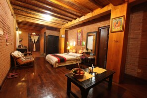 A cozy room with a wooden ceiling, a bed with a red and black bedspread, a wicker chair, and a table with a basket of fruit.