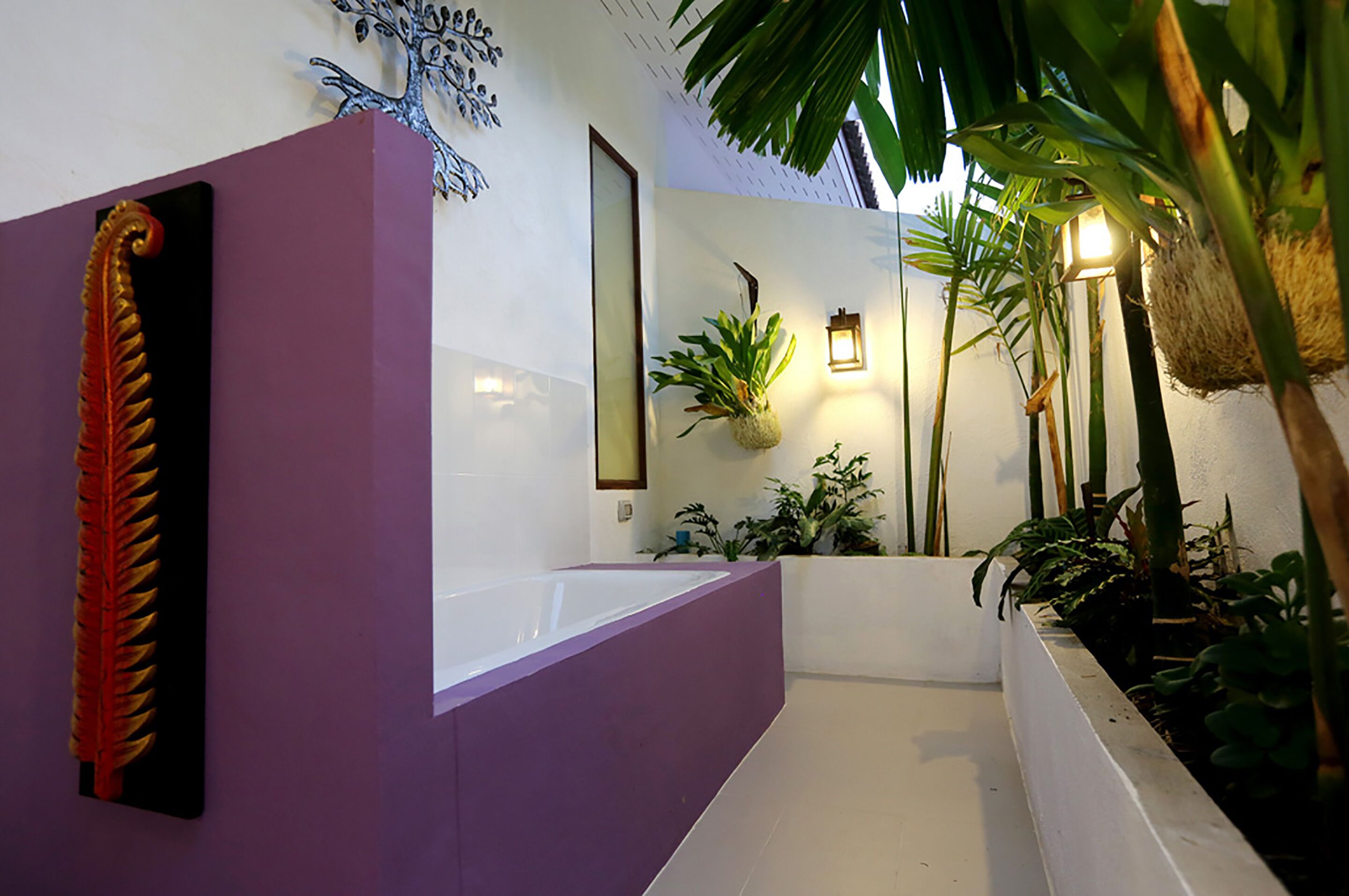Un baño moderno con una pared de acento púrpura, una bañera blanca y una planta en maceta.