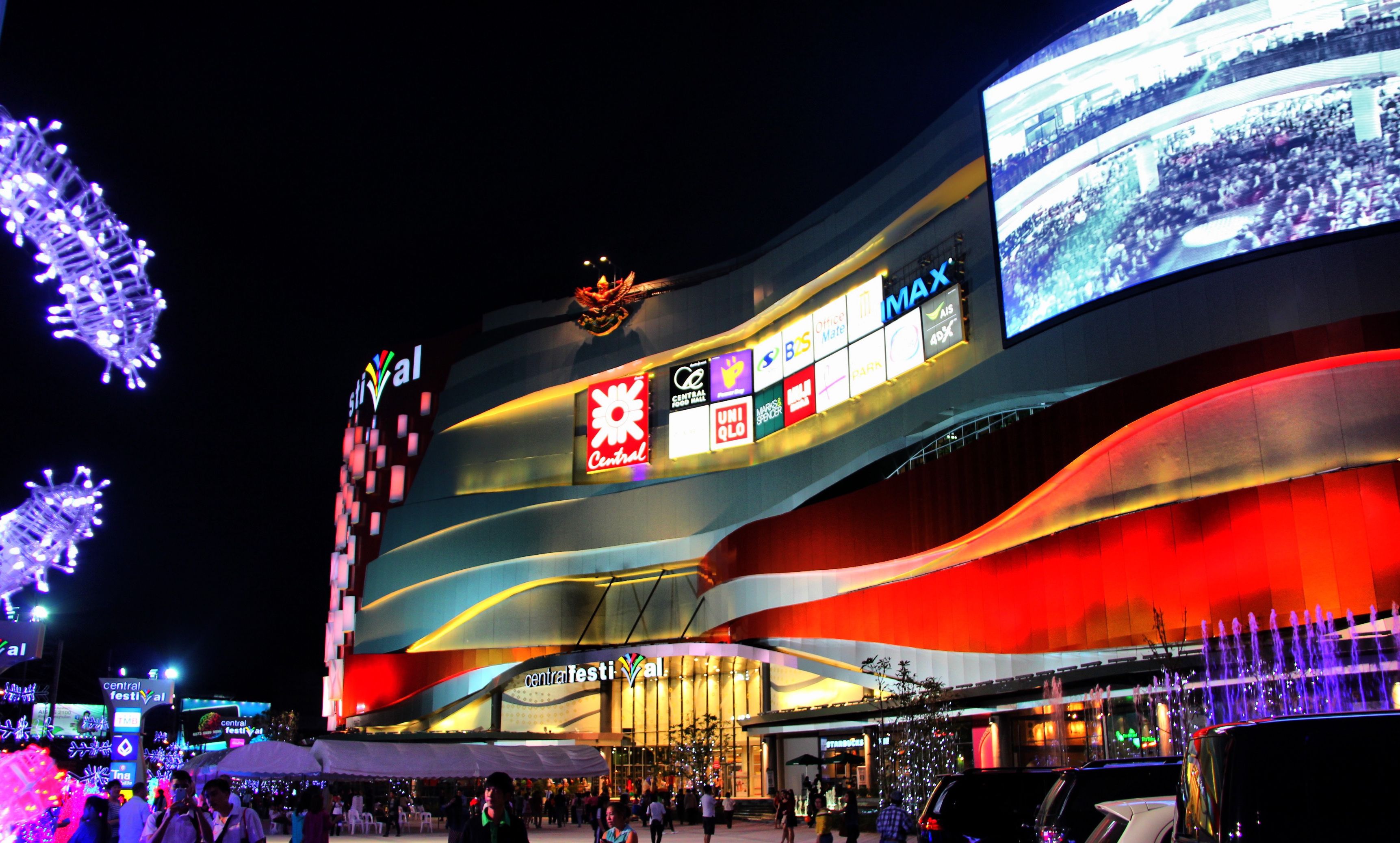 A building with a curved facade, multiple illuminated signs, and a large screen displaying an event.