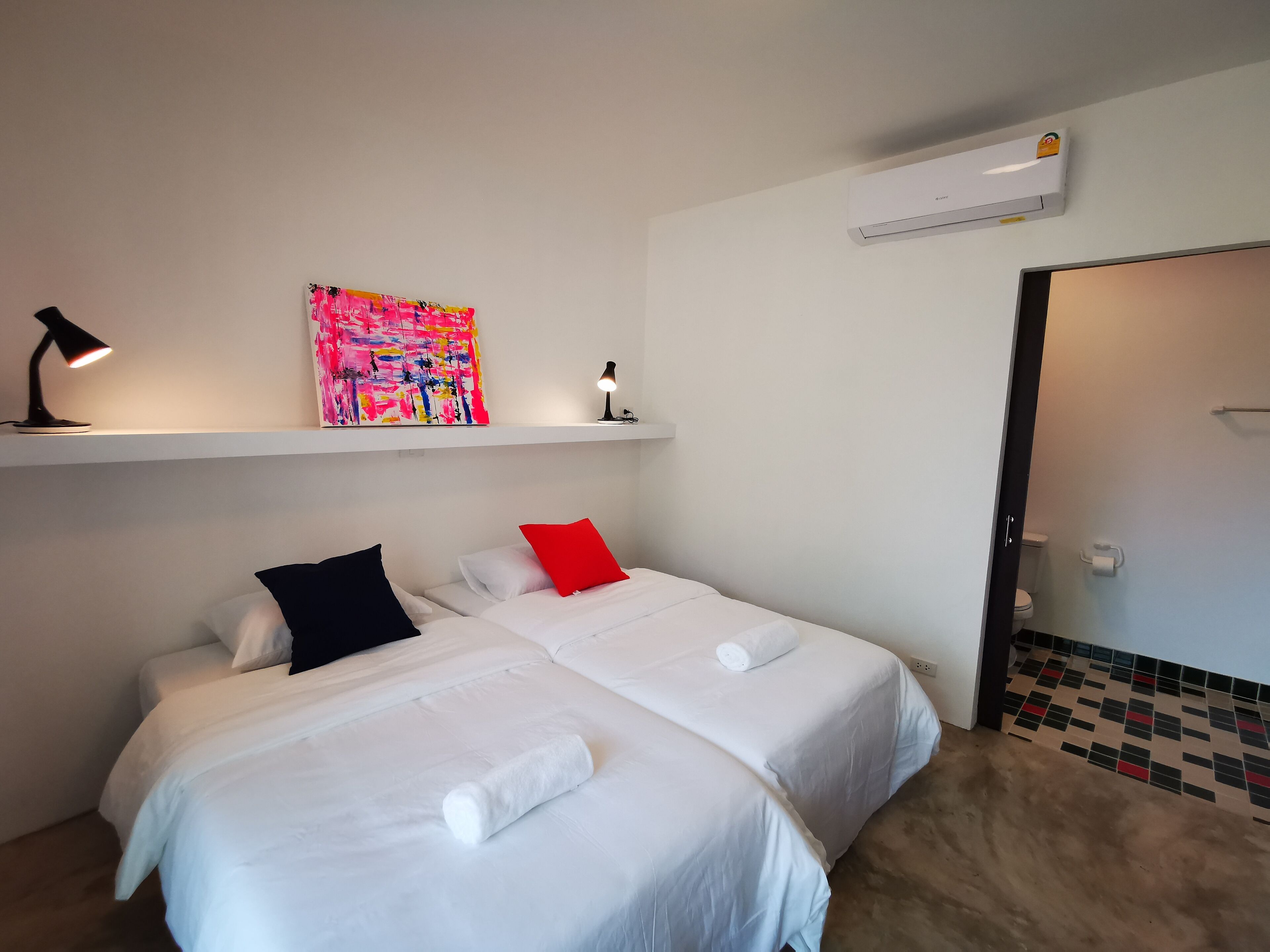 A hotel room with two beds, a colorful abstract painting, a white air conditioner, and a tiled floor.