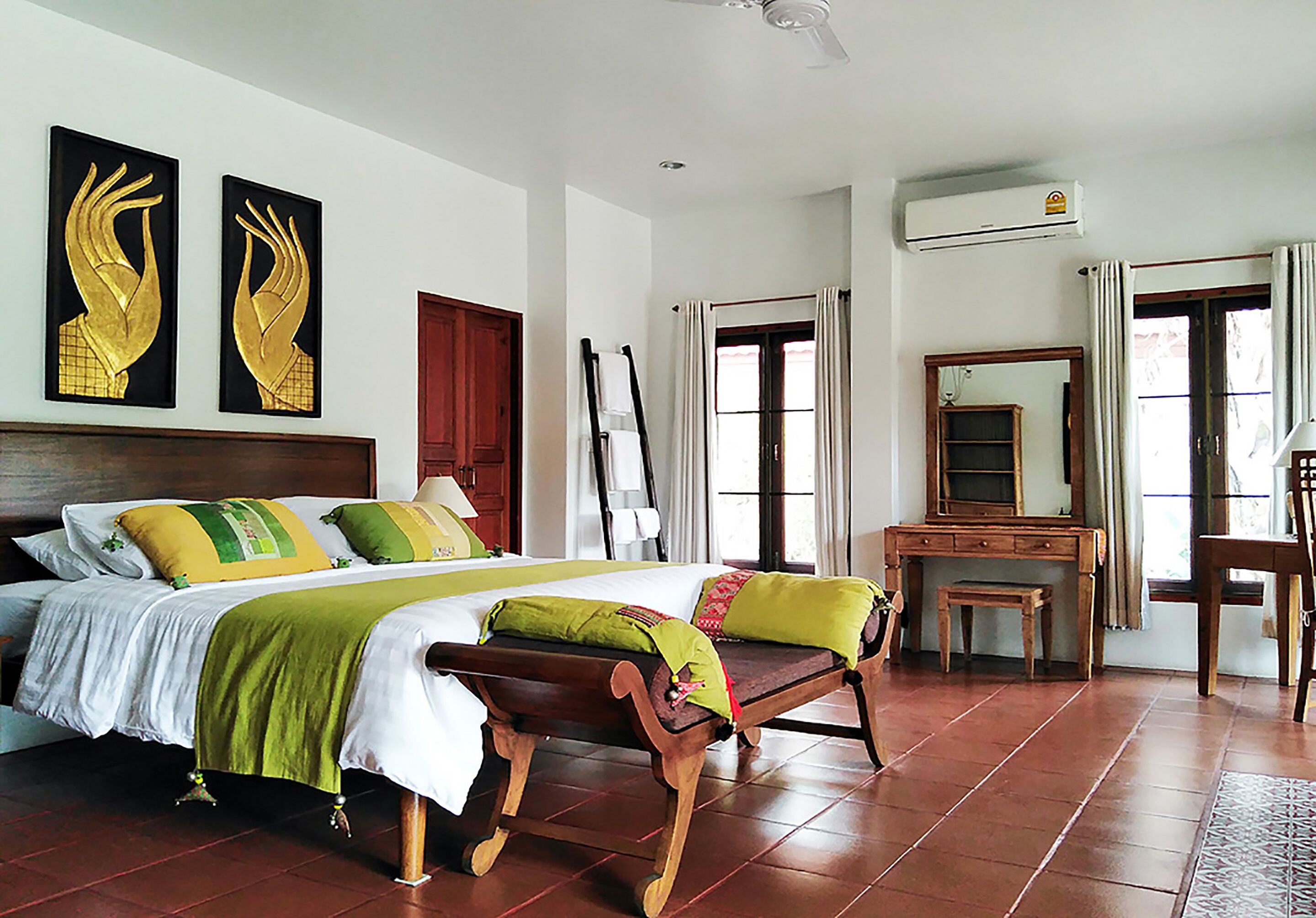 A spacious bedroom with a large bed, a wooden bench, a desk, and a mirror.