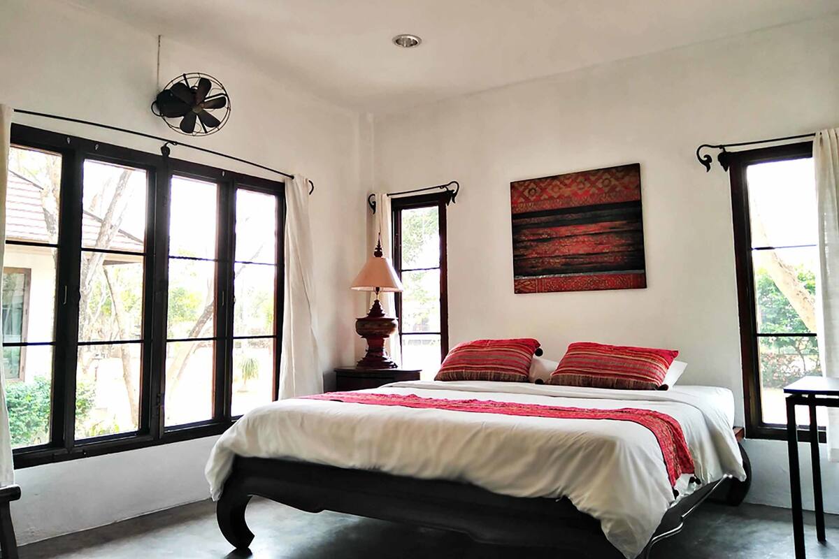 A bedroom with a bed, a ceiling fan, a window, and a wall-mounted lamp.