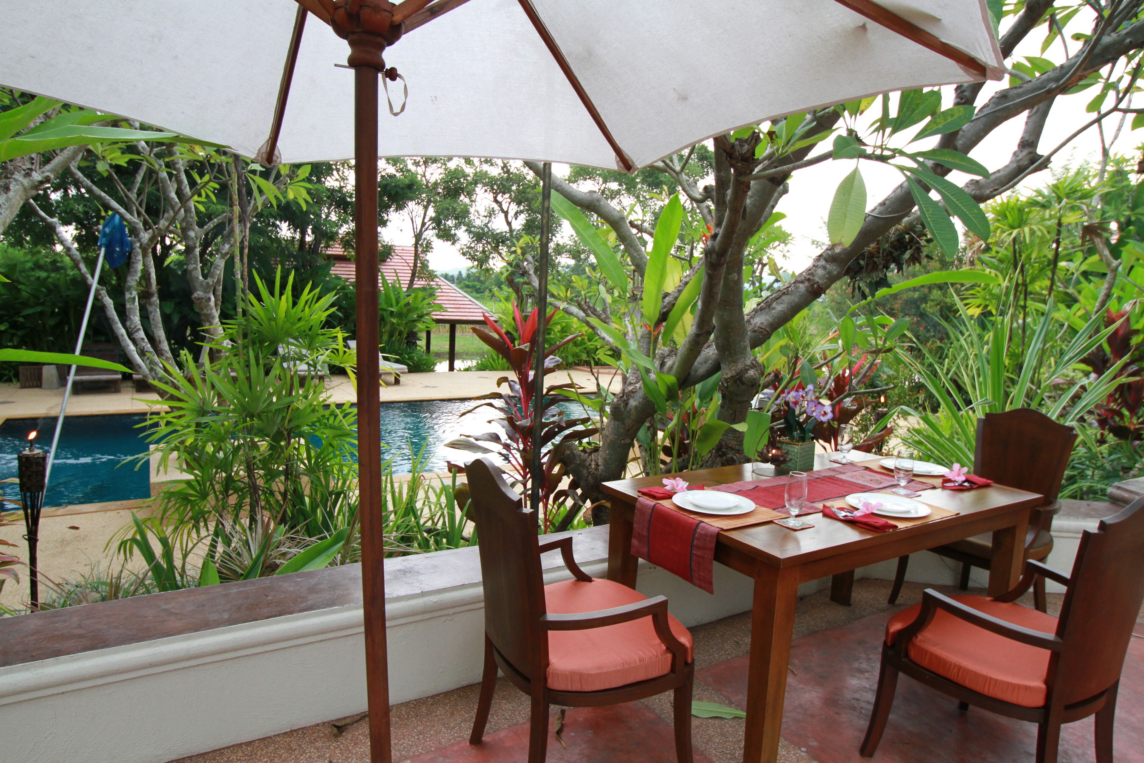An outdoor dining area with a table set for four, surrounded by chairs, under a large umbrella.