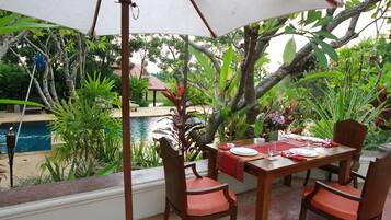 An outdoor dining area with a table set for four, surrounded by chairs, under a large umbrella.