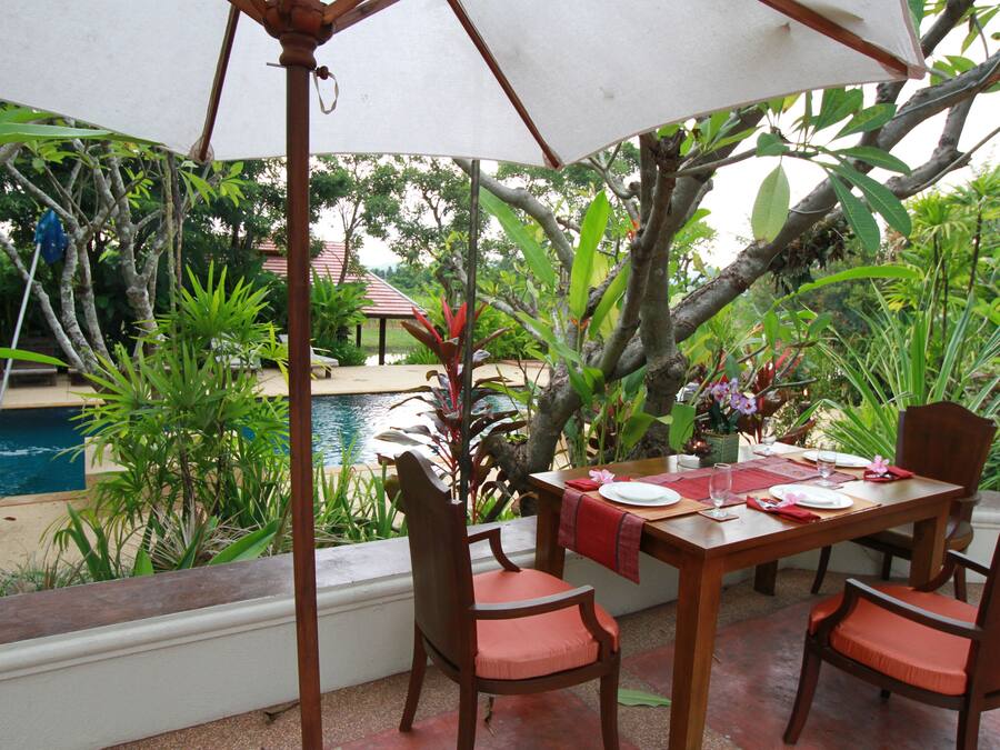 An outdoor dining area with a table set for four, surrounded by chairs, under a large umbrella.