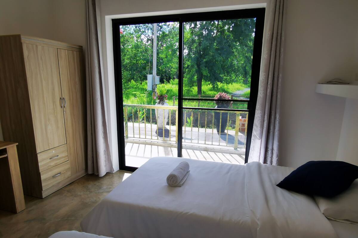 A bedroom with a bed, a wardrobe, and a balcony with a view of greenery.