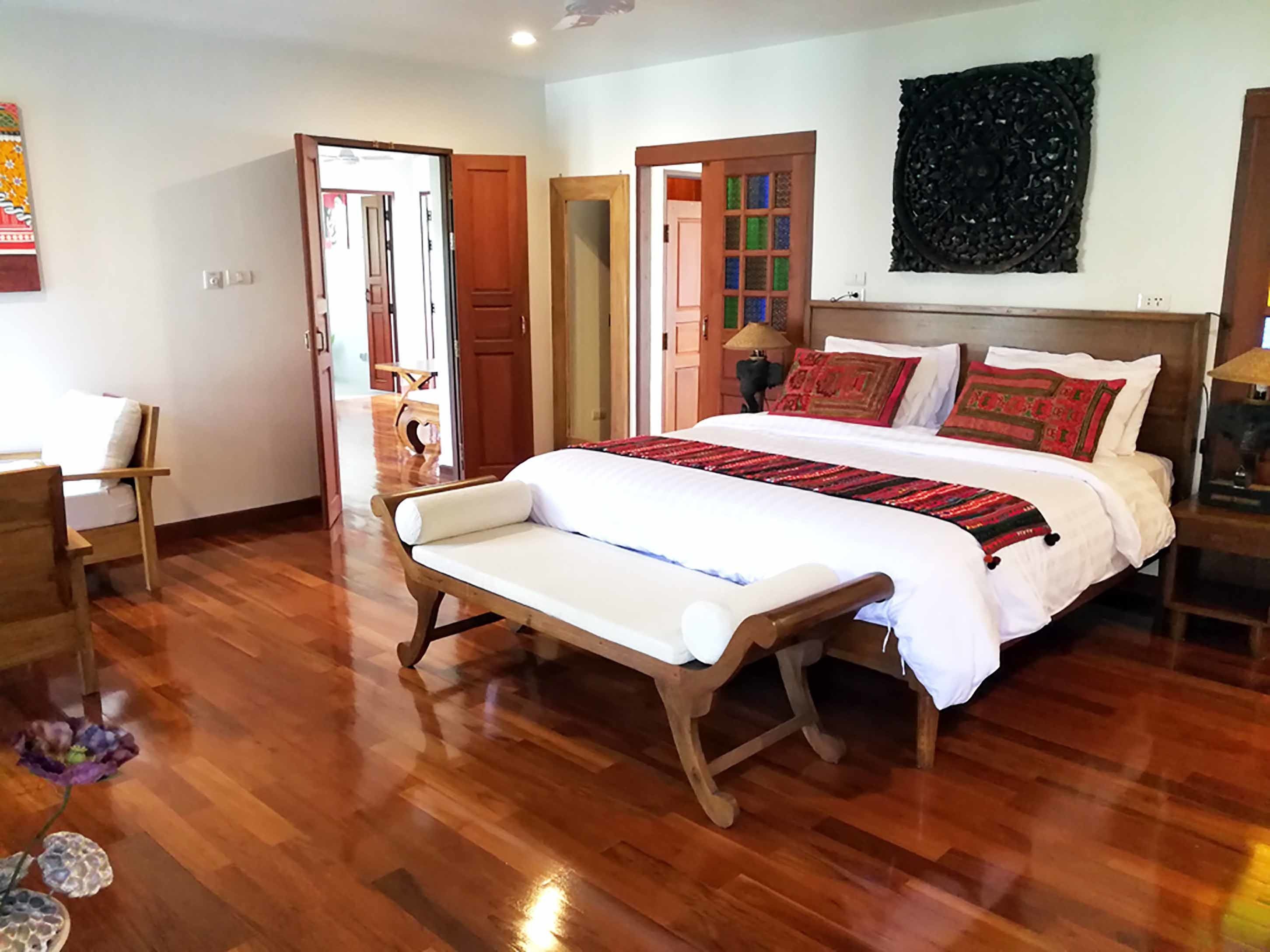 Un dormitorio con suelo de madera, cama con ropa blanca y roja, un banco y una obra de arte colgada en la pared.