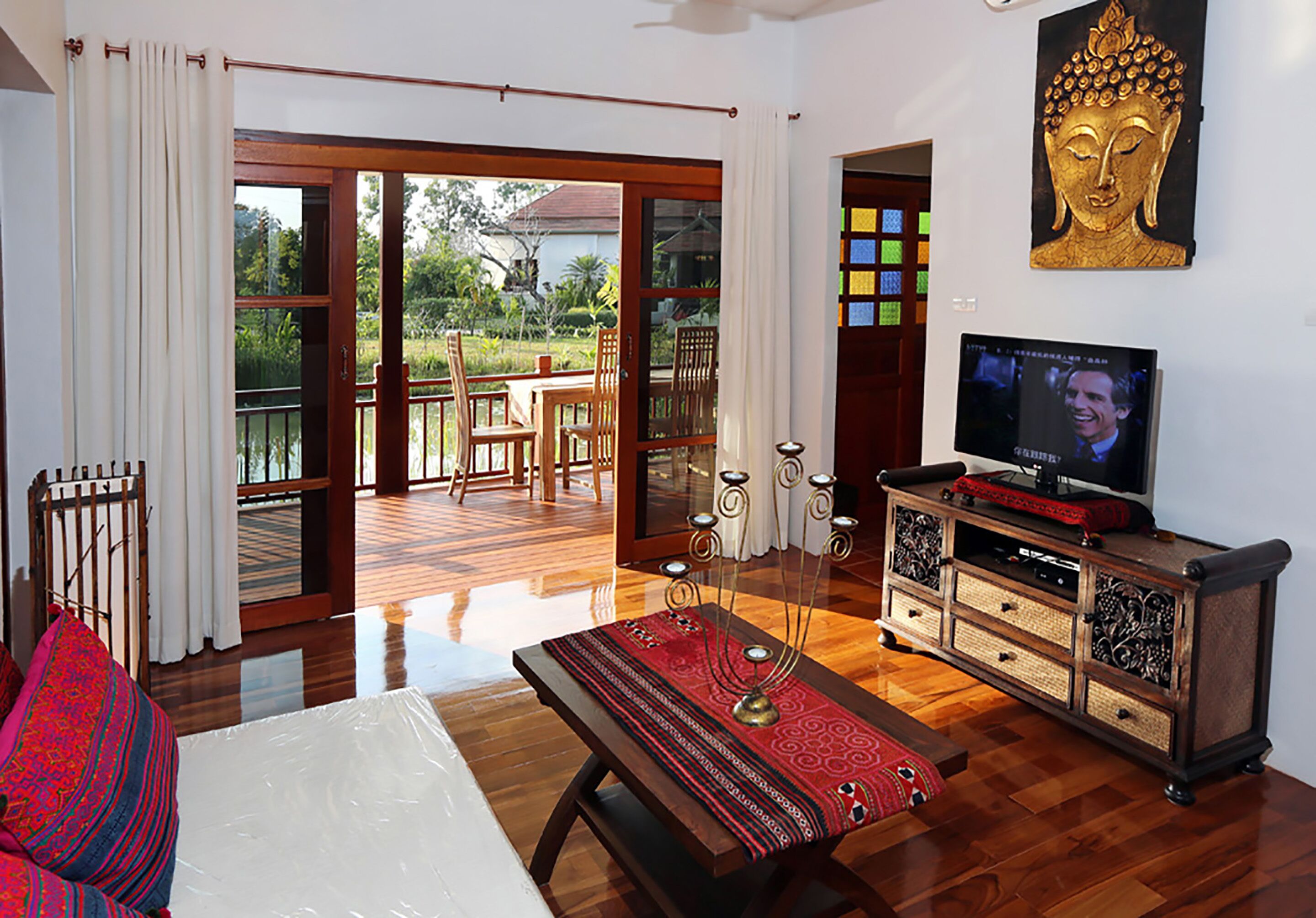 A room with a bed, a TV, a wooden cabinet, and a view of a garden through a glass door.