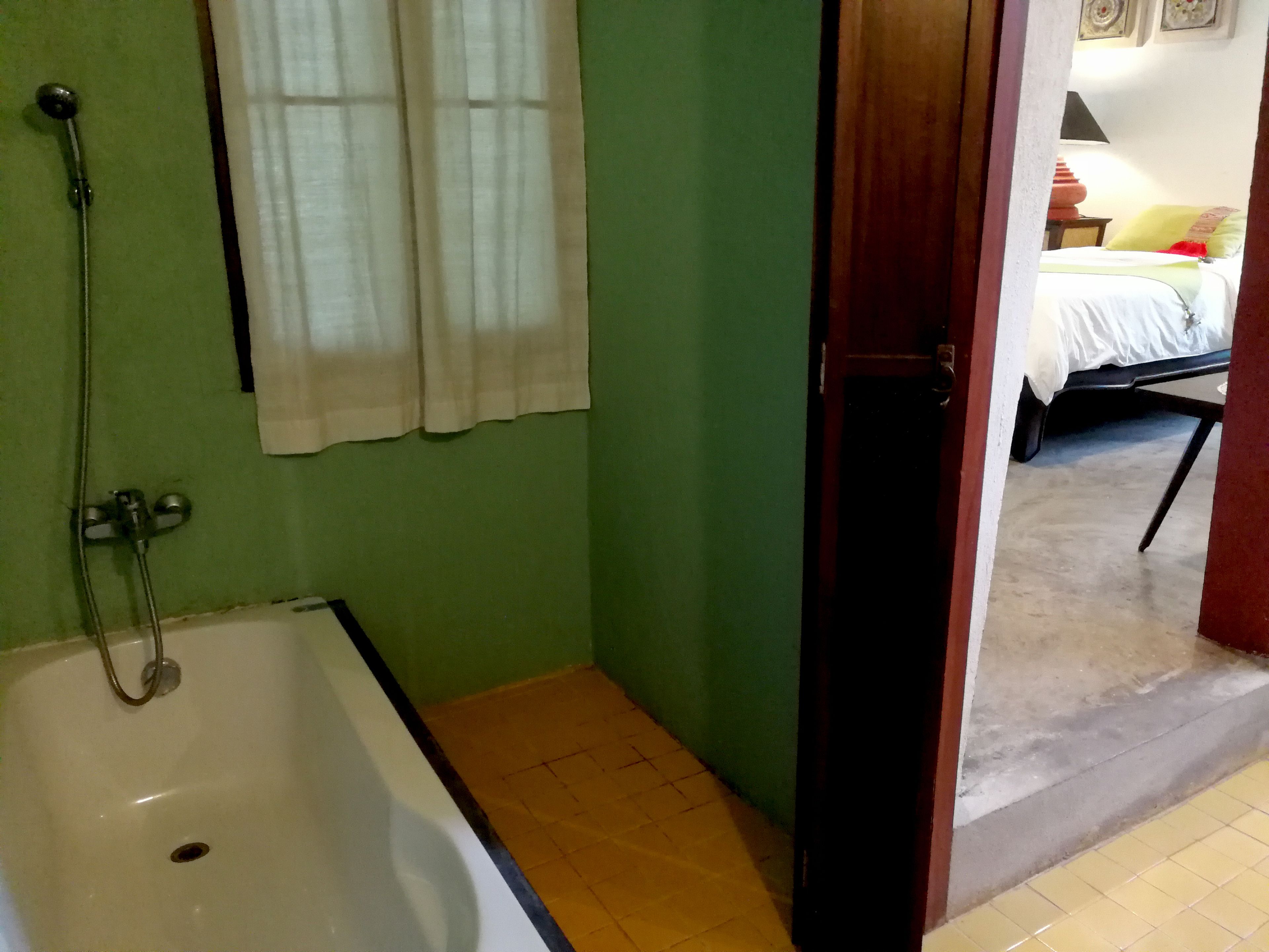 A bathroom with a bathtub, a shower, and a window with curtains.