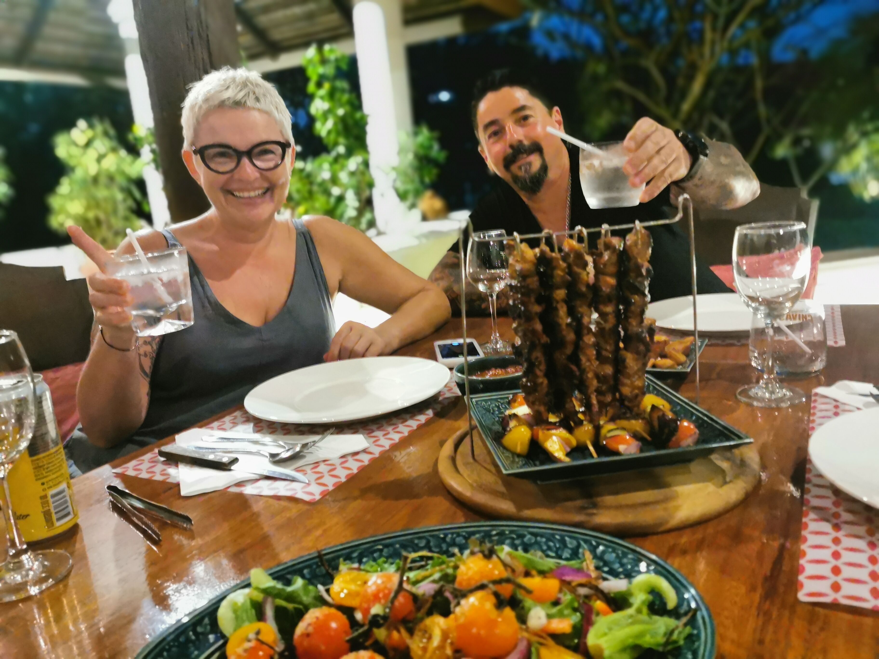 Une table à manger dressée avec une variété de plats, notamment des viandes grillées en brochettes et une salade.