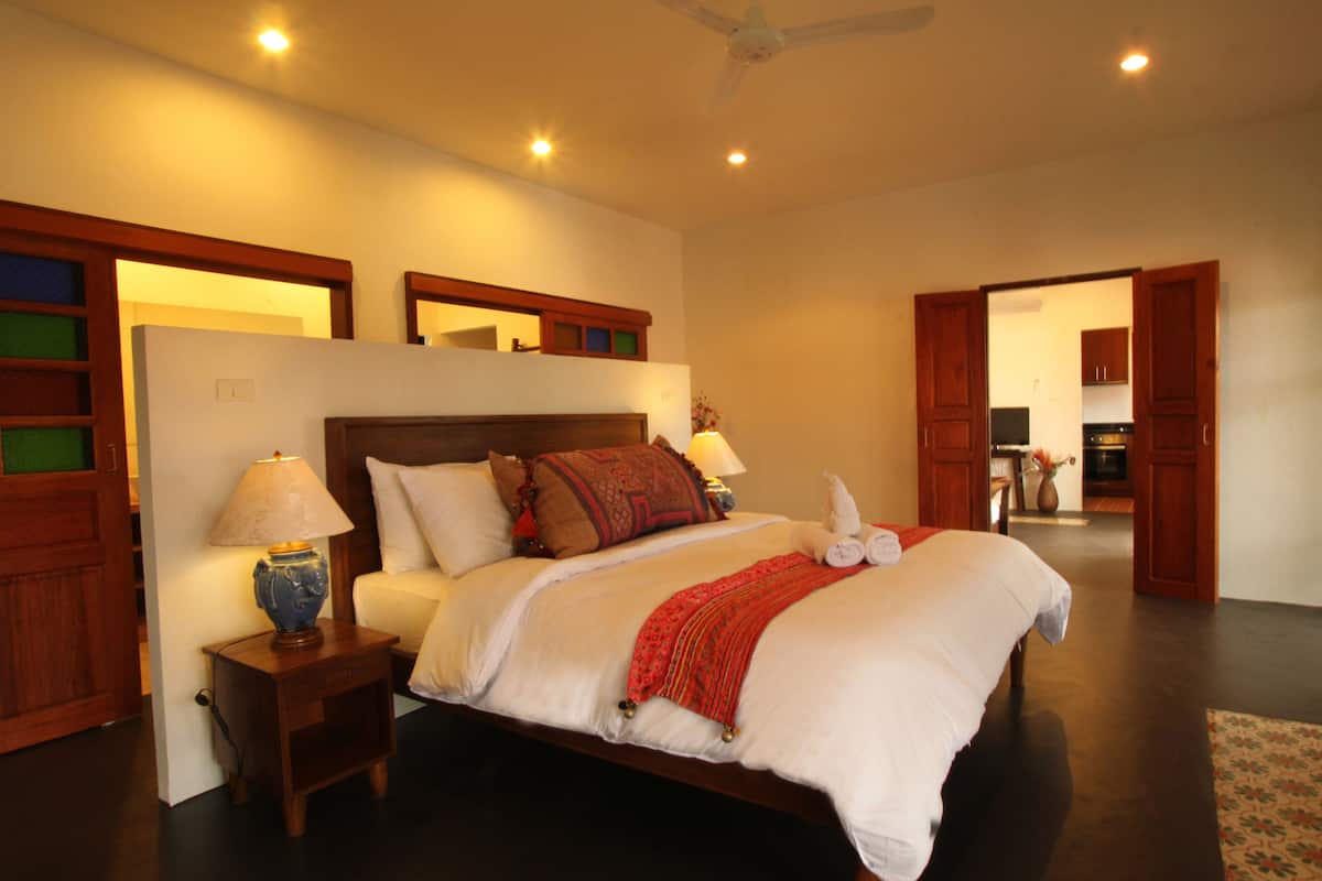 A spacious bedroom with a large bed, bedside lamps, and a wooden headboard.