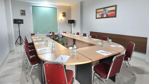 A conference room with a long table, red chairs, and water bottles. - Paramita Hotel (Pekanbaru)