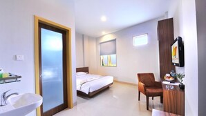 A hotel room with a bed, a desk with a chair, a TV, a sink, and a window with blinds. - Paramita Hotel (Pekanbaru)