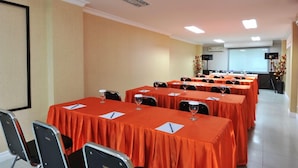 A conference room with multiple tables covered in orange tablecloths, equipped with chairs and wine glasses. - Gaja Hotel (Pekanbaru)