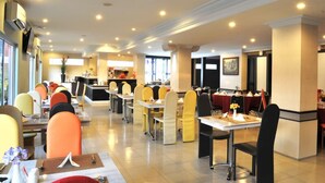A spacious dining area with multiple tables and chairs, a central counter, and large windows providing natural light. - Gaja Hotel (Pekanbaru)