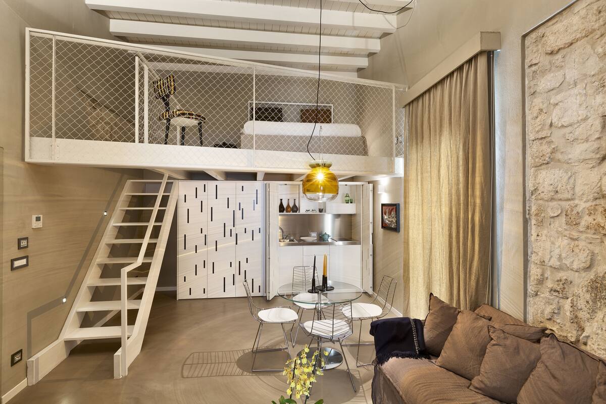 A modern interior with a loft bedroom, a dining area, and a staircase.