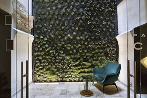 Ein modernes Interieur mit einer strukturierten Wand, einem Glastisch und einem blaugrünen Stuhl.